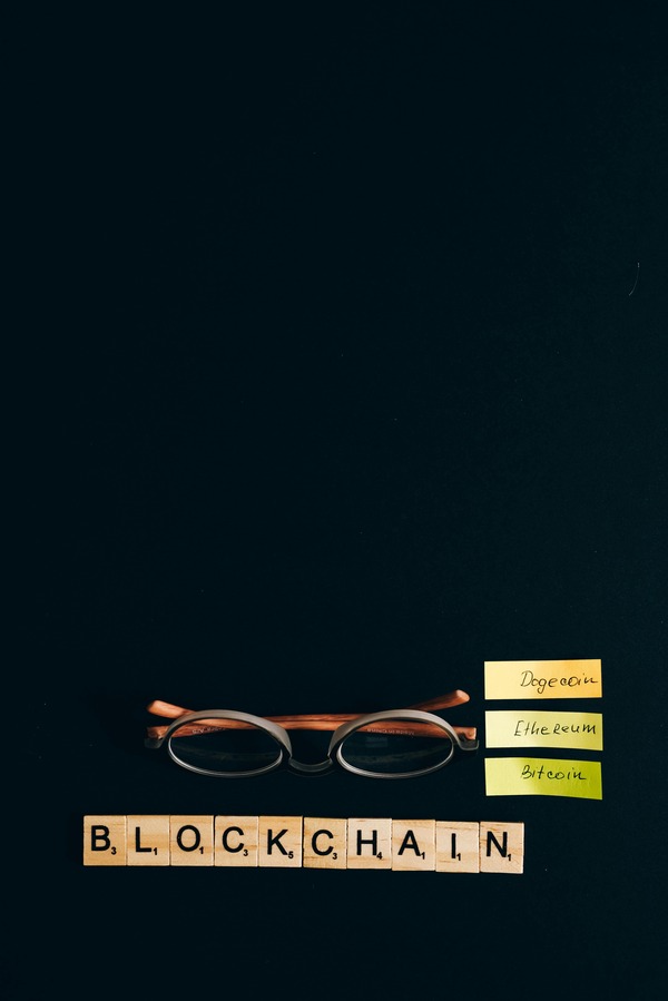 Reading glasses and sticky notes with cryptocurrency names next to BLOCKCHAIN letter tiles on a dark background