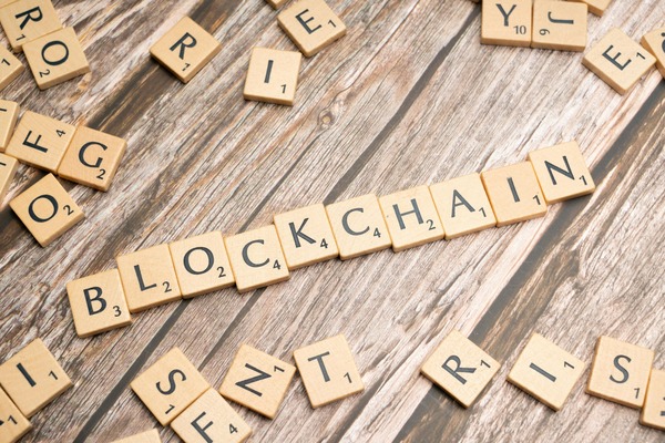 Wooden tiles spelling BLOCKCHAIN next to glasses and sticky notes with cryptocurrency names
